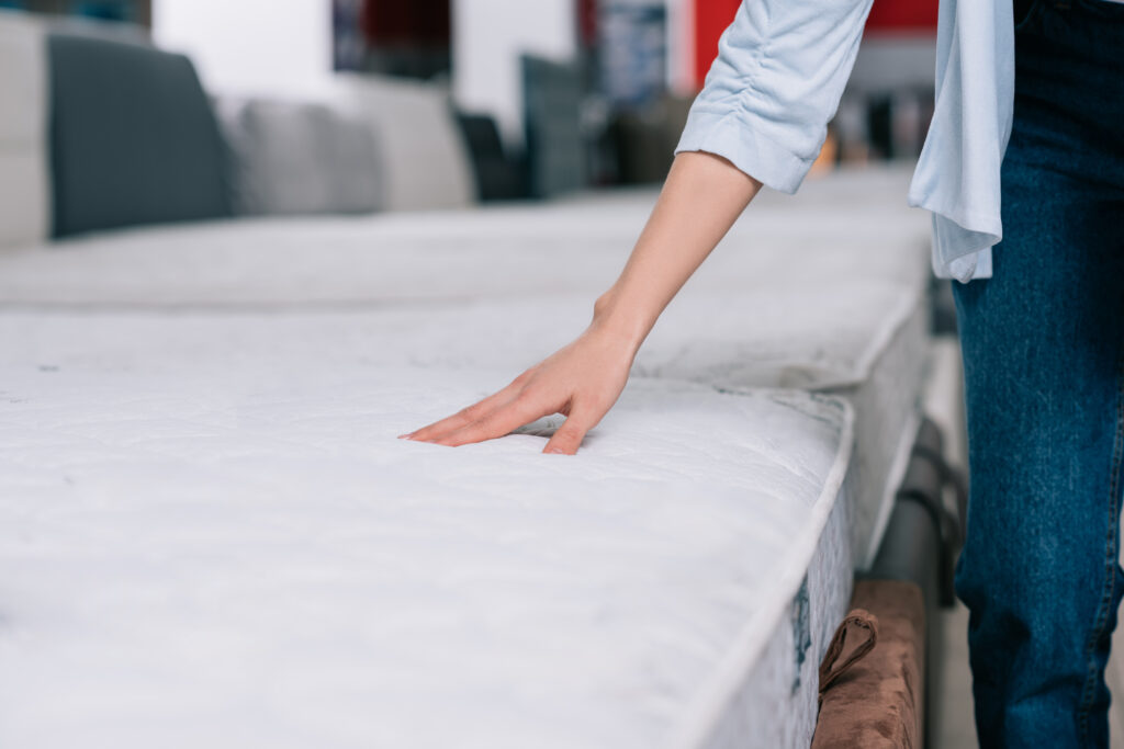 Signs Your Mattress Is Causing Your Back Pains - partial view of woman touching orthopedic mattress in furniture shop