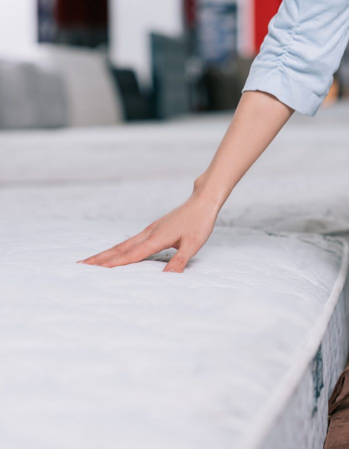 Beds Galore – Signs Your Mattress Is Causing Your Back Pains Signs Your Mattress Is Causing Your Back Pains - partial view of woman touching orthopedic mattress in furniture shop