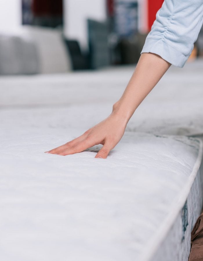 Signs Your Mattress Is Causing Your Back Pains - partial view of woman touching orthopedic mattress in furniture shop